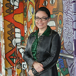 Woman (Melissa Simon) in a leather coat in front of a colorful mural.