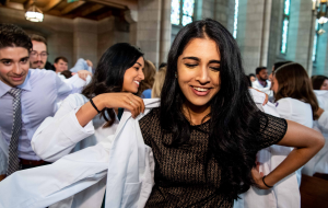 Group of people in a church. Woman in foreground is helped into a white coat. 