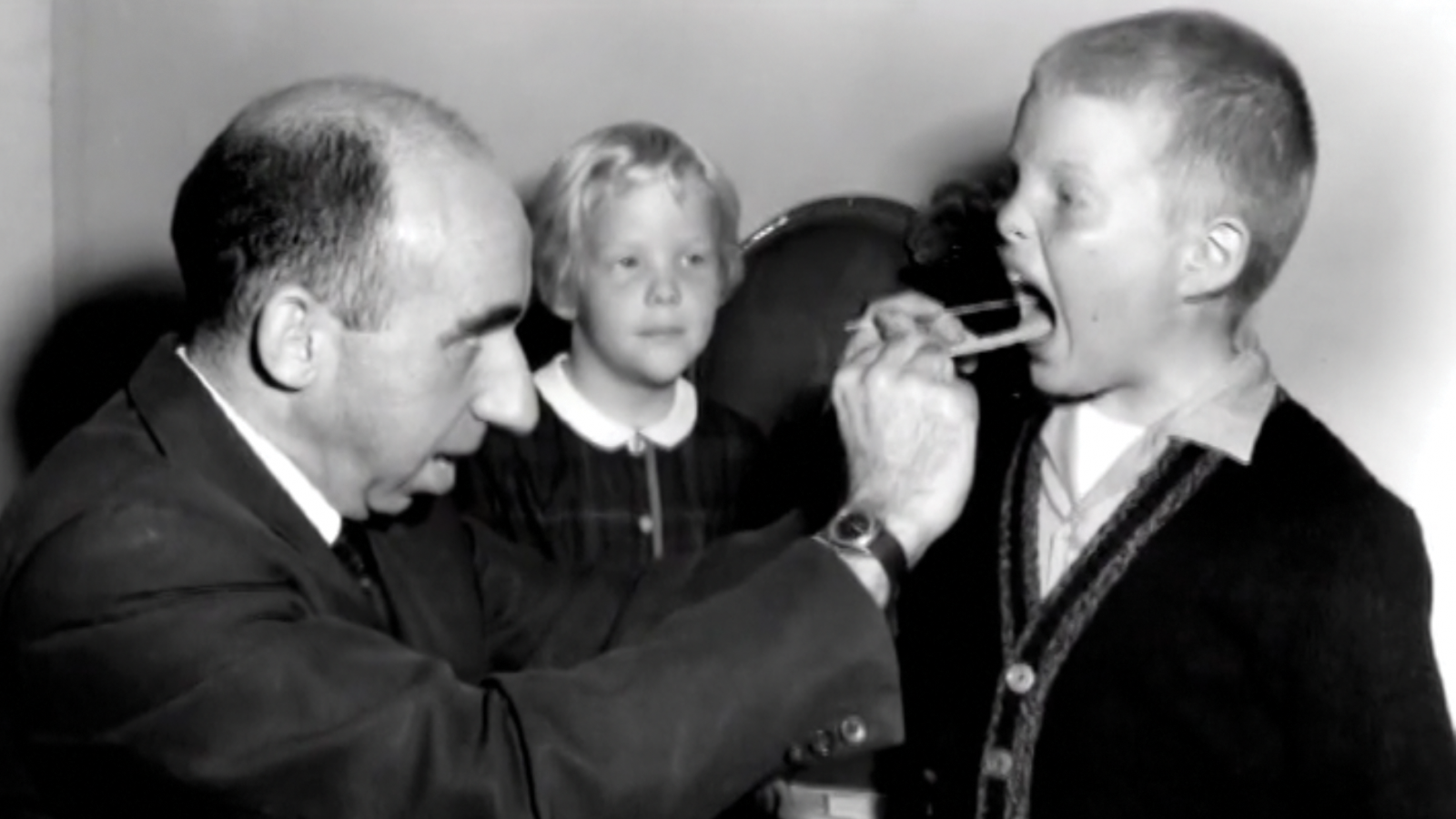 Dr. Stamler examining the throat of a young boy while a young girl watches.