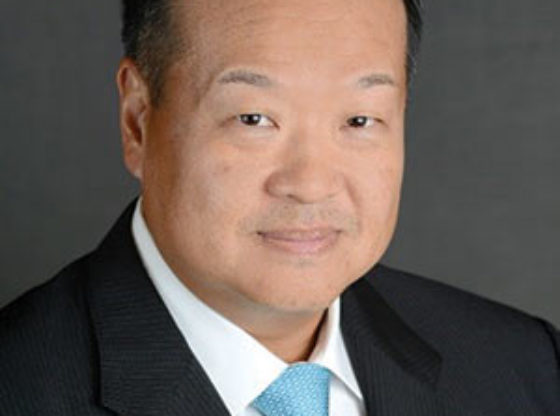 Headshot of man wearing a dark suit jacket and a blue necktie.