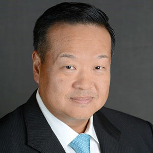 Headshot of man wearing a dark suit jacket and a blue necktie.